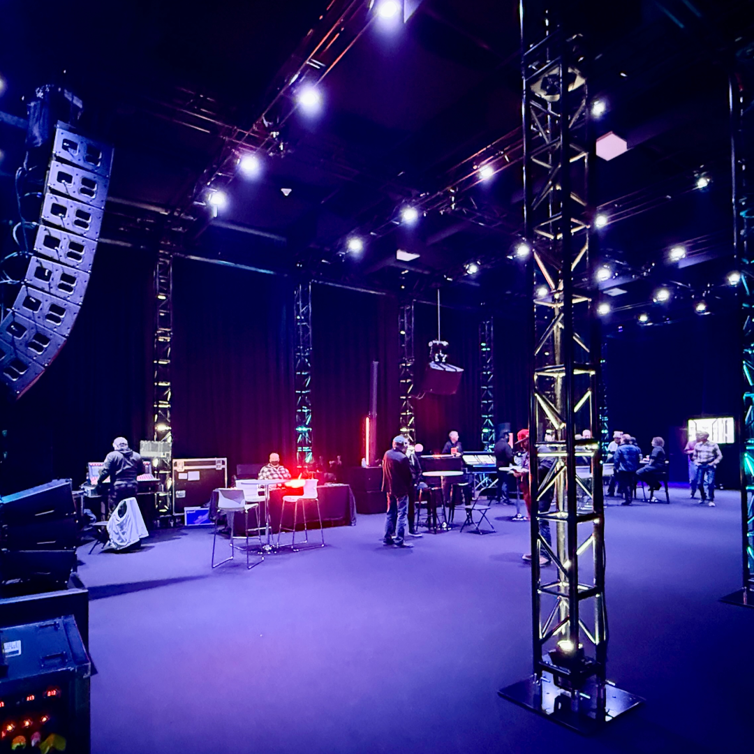 LPG-Party-25-Studiosq Professional virtual studio setup in a black-draped production space featuring a curved LED video wall branded ‘LEGACY Production Group’, two high-definition broadcast cameras on tripods with attached monitors and cables, and surrounding studio lighting, ready for live streaming or virtual event production