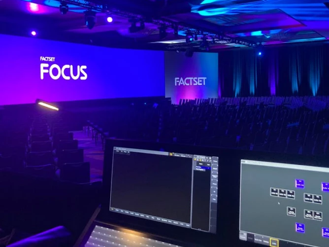 about-our-approach-partnership Panoramic curved LED video wall wrapping three sides of a hotel ballroom stage, displaying a multi-colored test-pattern grid of red, green, blue, cyan, magenta, and yellow bars for pixel calibration, under a flown truss lighting grid and crystal chandelier
